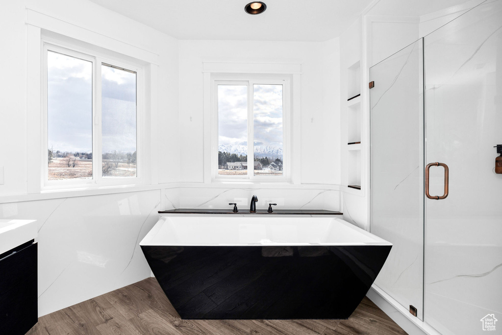 Full bath featuring built in shelves, a stall shower, a soaking tub, and wood finished floors