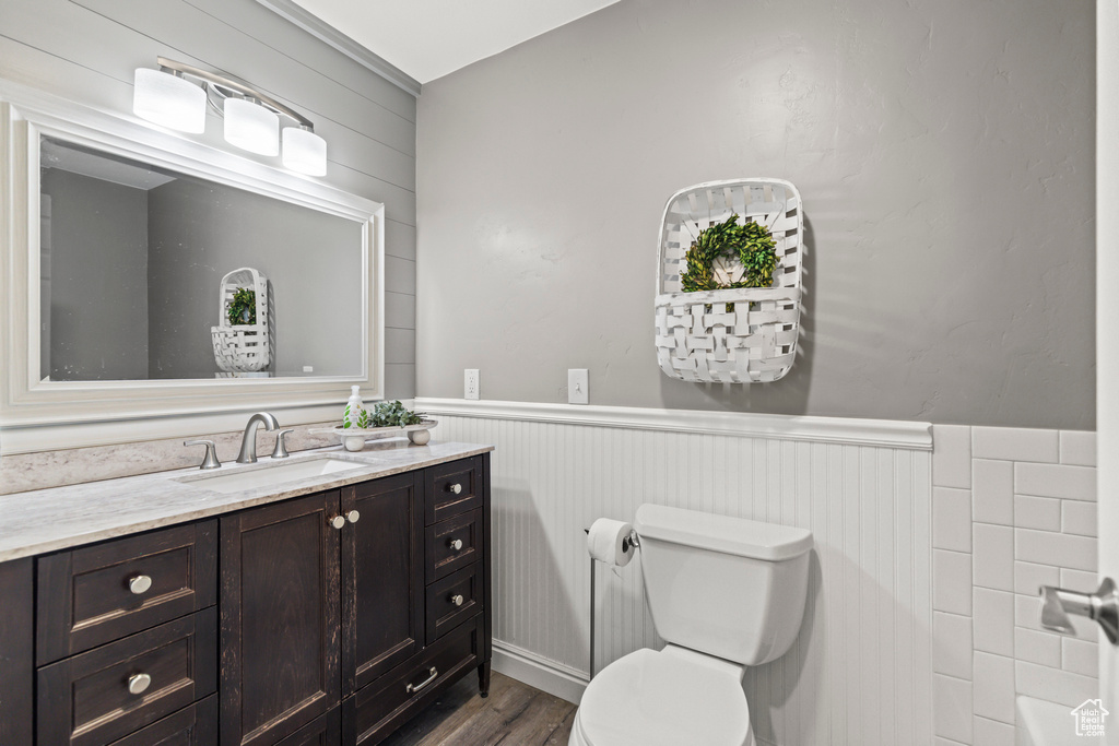 Bathroom with a wainscoted wall, vanity, toilet, and wood finished floors