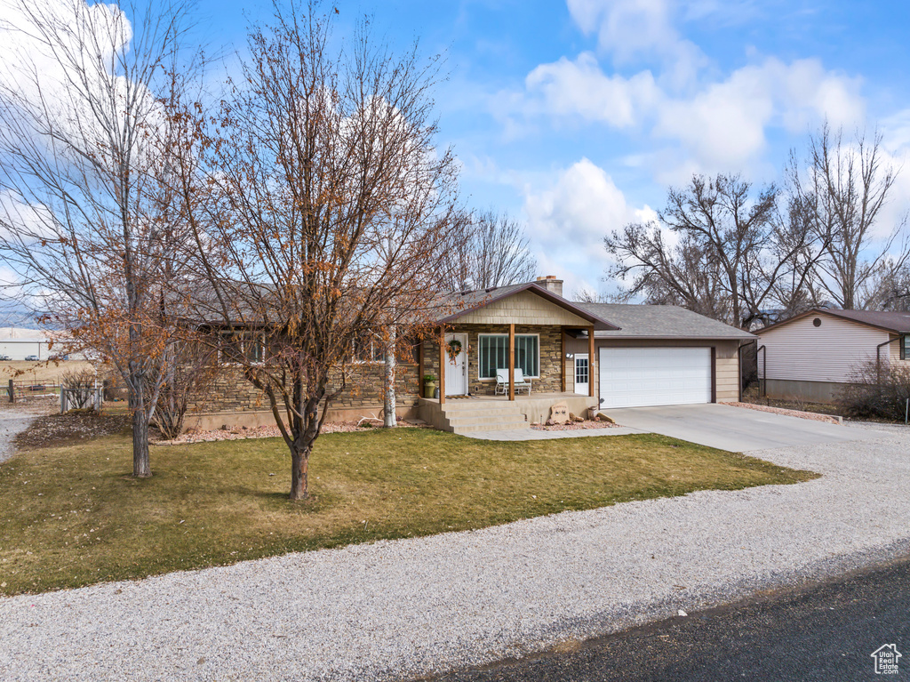 Ranch-style home featuring a garage, concrete driveway, stone siding, a chimney, and a front yard