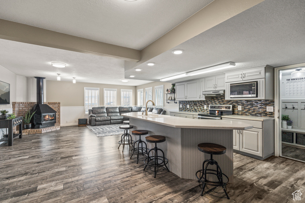 Kitchen with wainscoting, stainless steel appliances, under cabinet range hood, a kitchen bar, and a sink
