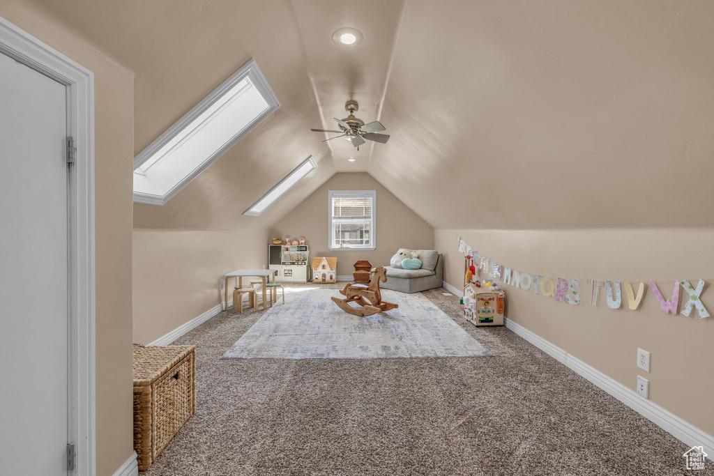 Playroom featuring carpet floors, vaulted ceiling with skylight, ceiling fan, and baseboards