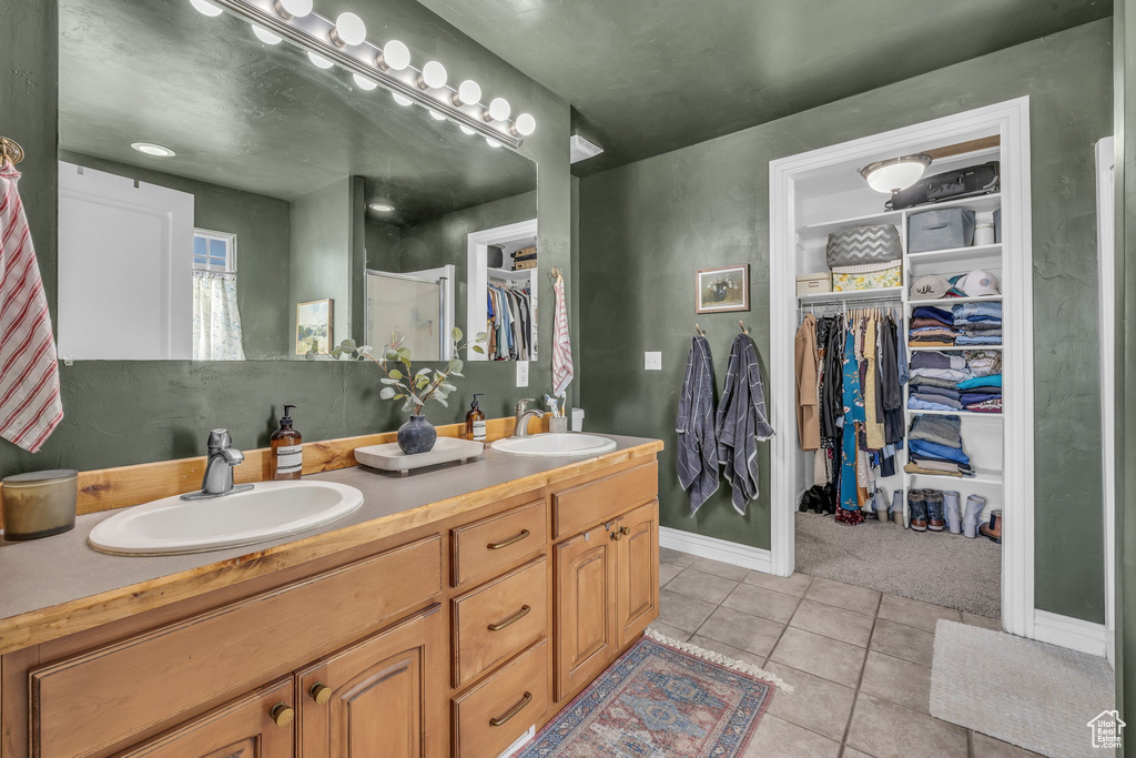 Bathroom featuring a walk in closet, double vanity, a sink, and tile patterned floors