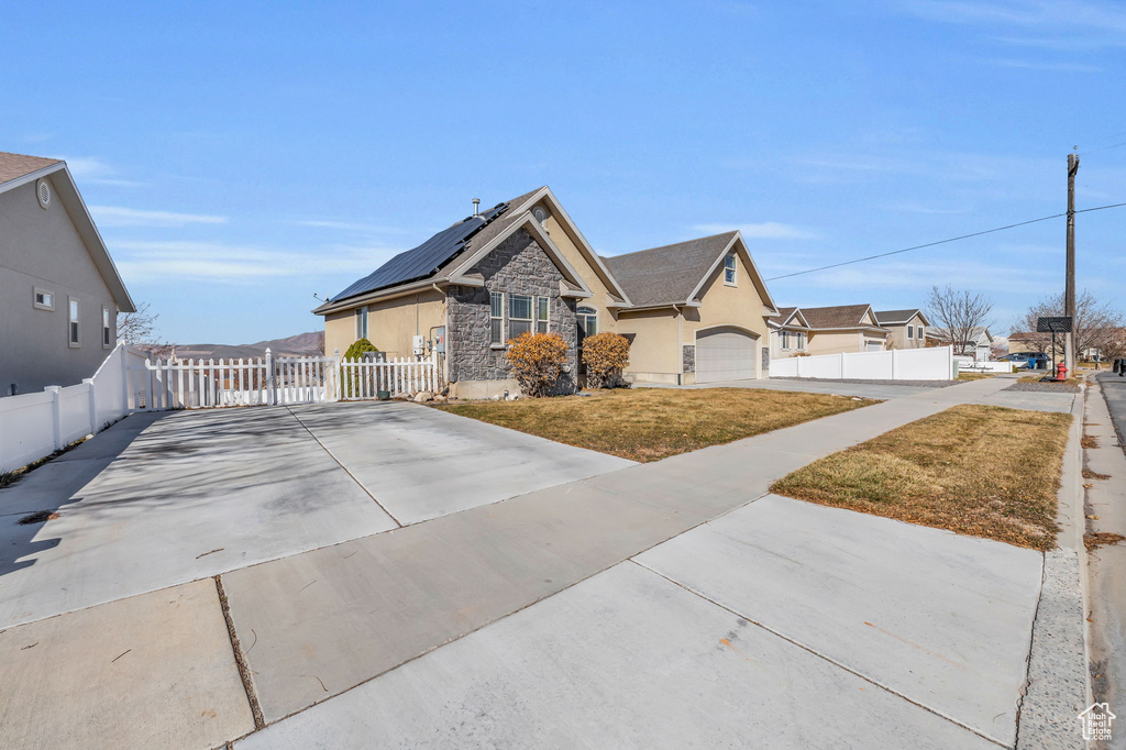 View of front of home with driveway, stone siding, fence, roof mounted solar panels, and a front lawn