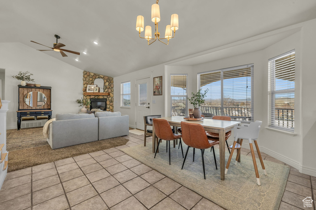 Dining area featuring light tile patterned flooring, ceiling fan with notable chandelier, a fireplace, baseboards, and vaulted ceiling