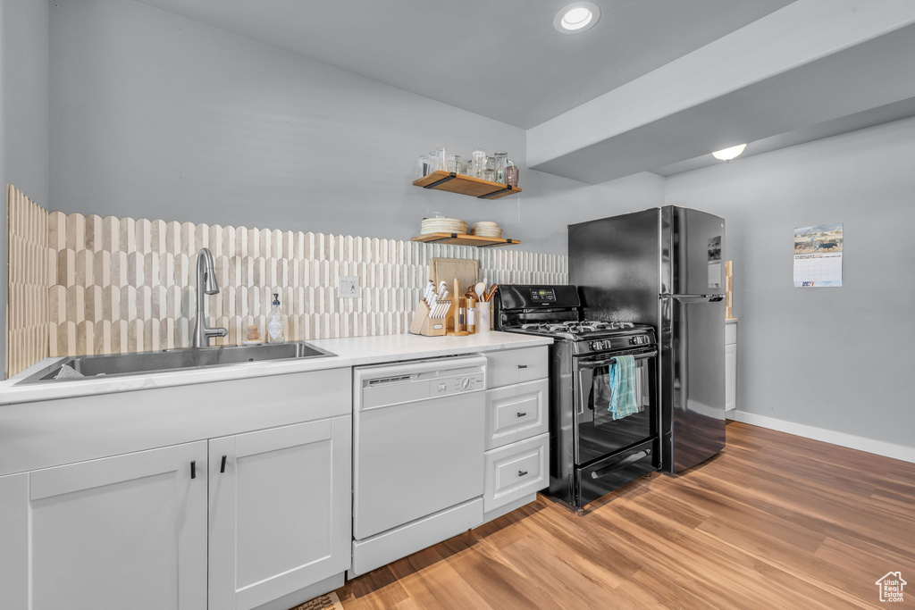 Kitchen with light wood-type flooring, black appliances, white cabinetry, open shelves, and a sink