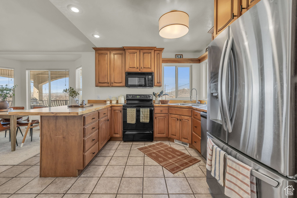 Kitchen featuring light countertops, light tile patterned flooring, a sink, a peninsula, and black appliances