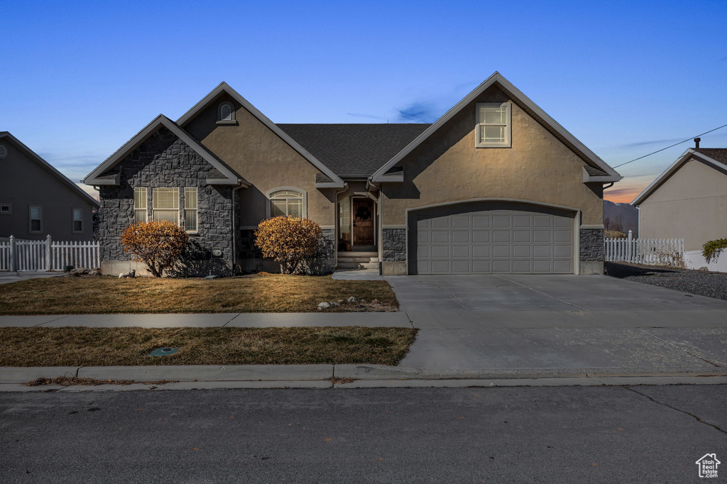 View of front of home featuring stucco siding, an attached garage, fence, stone siding, and driveway