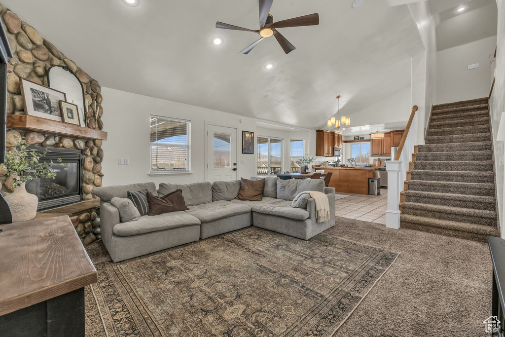 Living area with high vaulted ceiling, a stone fireplace, recessed lighting, ceiling fan with notable chandelier, and stairs