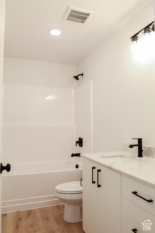 Full bathroom featuring shower / washtub combination, visible vents, toilet, vanity, and wood finished floors