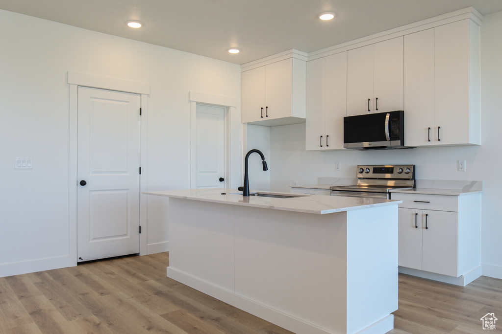 Kitchen with a center island with sink, stainless steel appliances, light wood-style floors, white cabinetry, and a sink