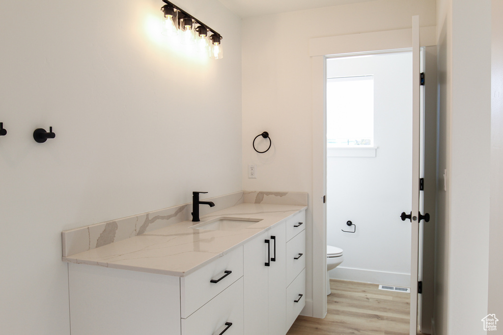 Bathroom with toilet, wood finished floors, visible vents, vanity, and baseboards