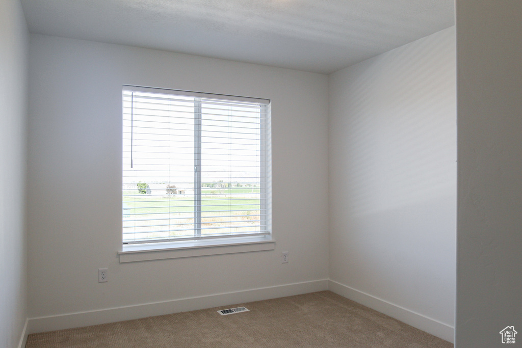 Unfurnished room featuring baseboards, visible vents, and light colored carpet
