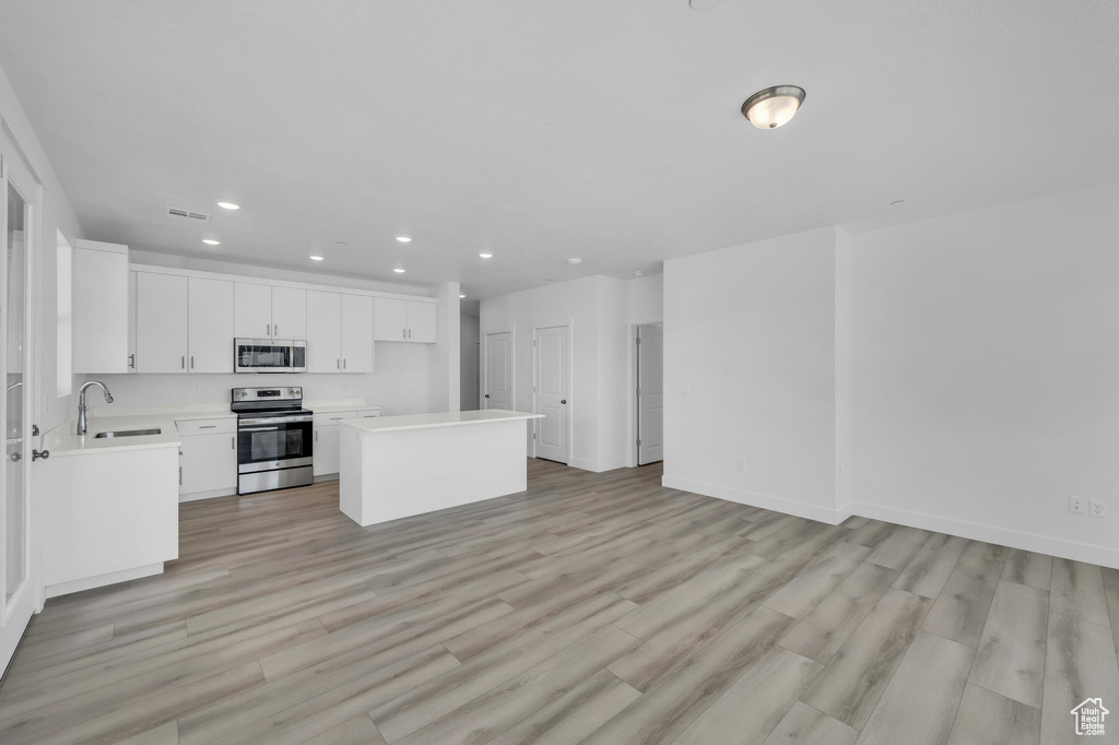 Kitchen featuring light wood-style flooring, stainless steel appliances, a sink, white cabinets, and light countertops