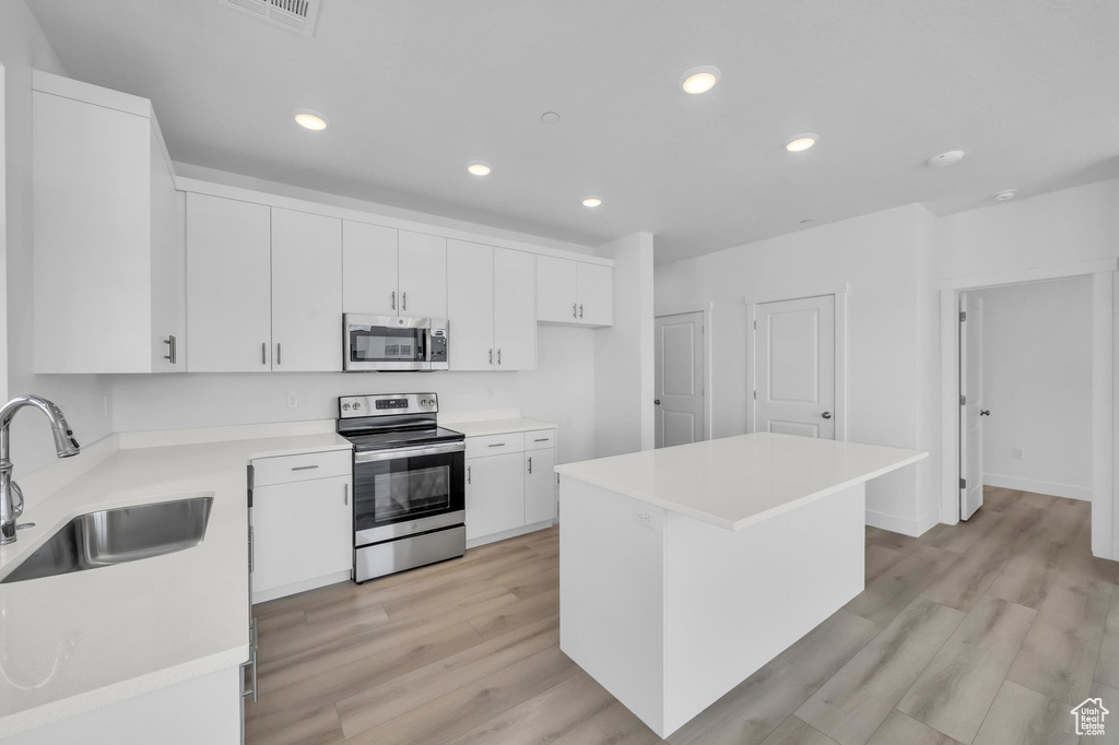 Kitchen with appliances with stainless steel finishes, light wood-type flooring, white cabinetry, a sink, and recessed lighting