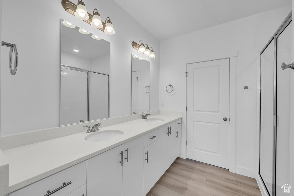 Full bathroom with double vanity, wood finished floors, a sink, and a shower stall
