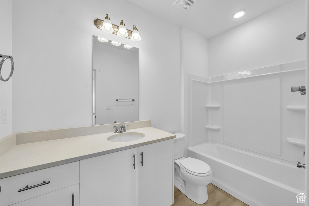 Bathroom featuring toilet, wood finished floors, visible vents, vanity, and shower / bathing tub combination