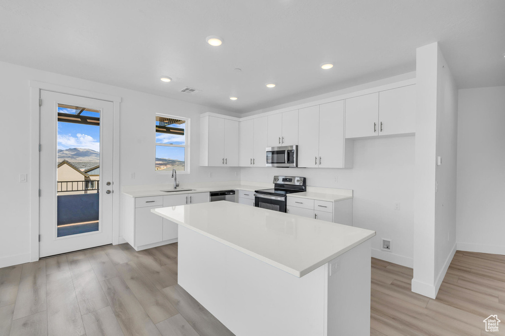 Kitchen featuring light wood-style flooring, a kitchen island, appliances with stainless steel finishes, light countertops, and a sink
