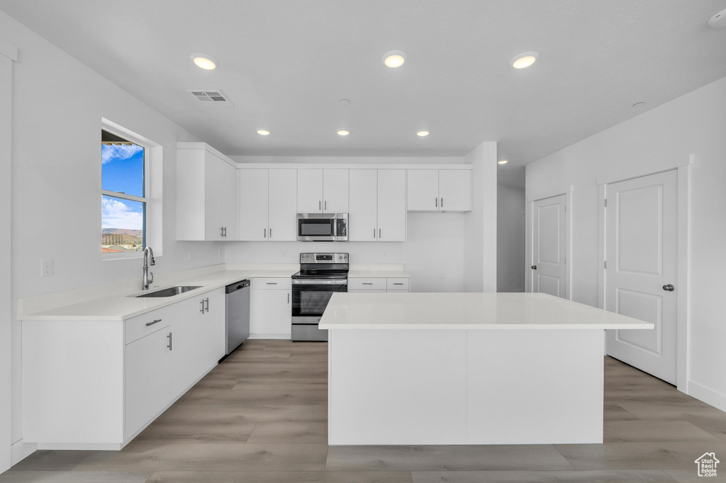Kitchen featuring a center island, stainless steel appliances, visible vents, white cabinets, and a sink