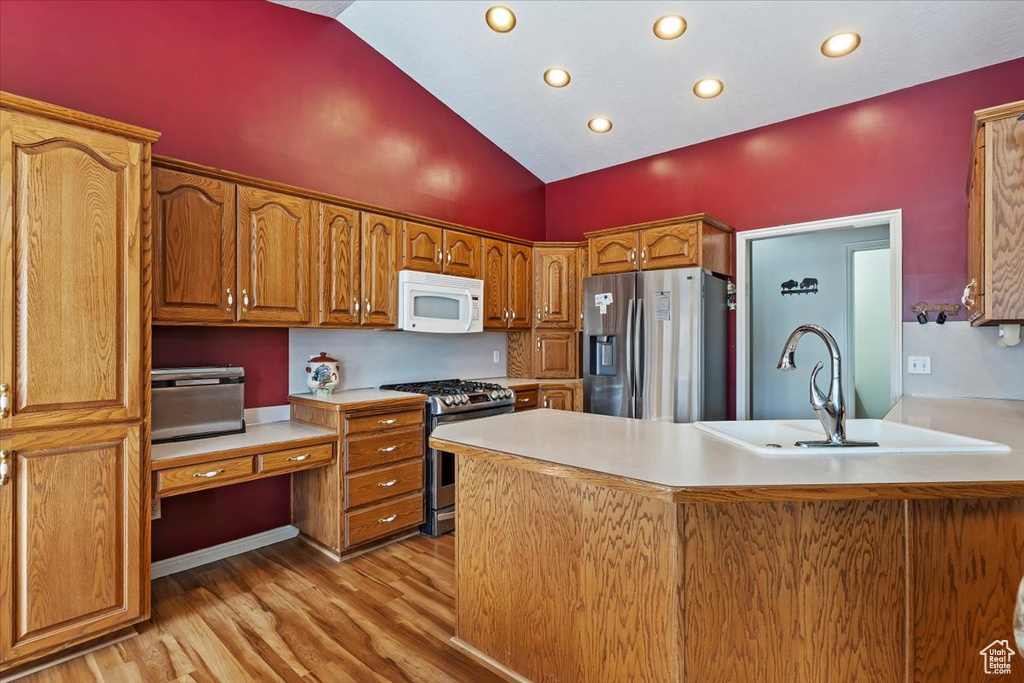 Kitchen featuring light wood finished floors, light countertops, appliances with stainless steel finishes, brown cabinetry, and a sink