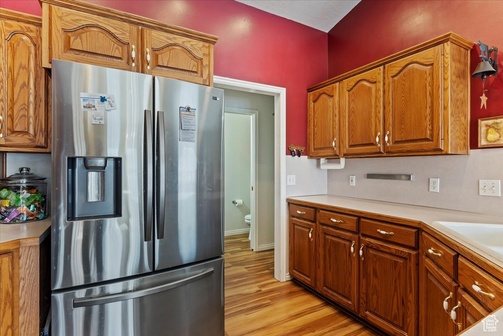 Kitchen featuring brown cabinetry, light countertops, stainless steel fridge, and light wood finished floors