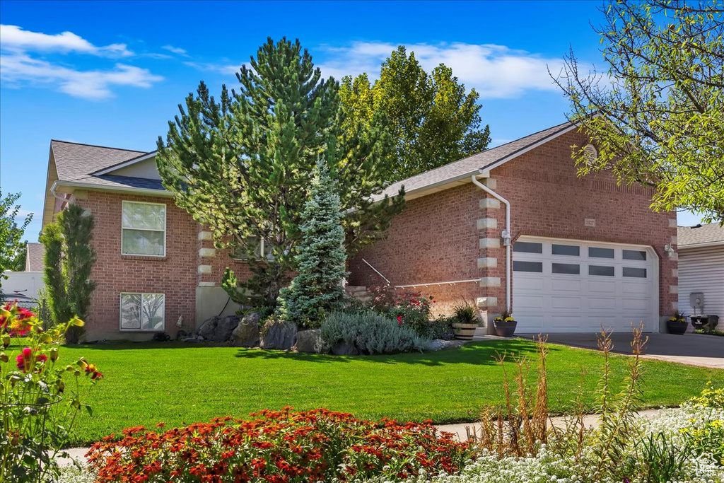 View of front of property featuring a garage, concrete driveway, brick siding, and a front lawn