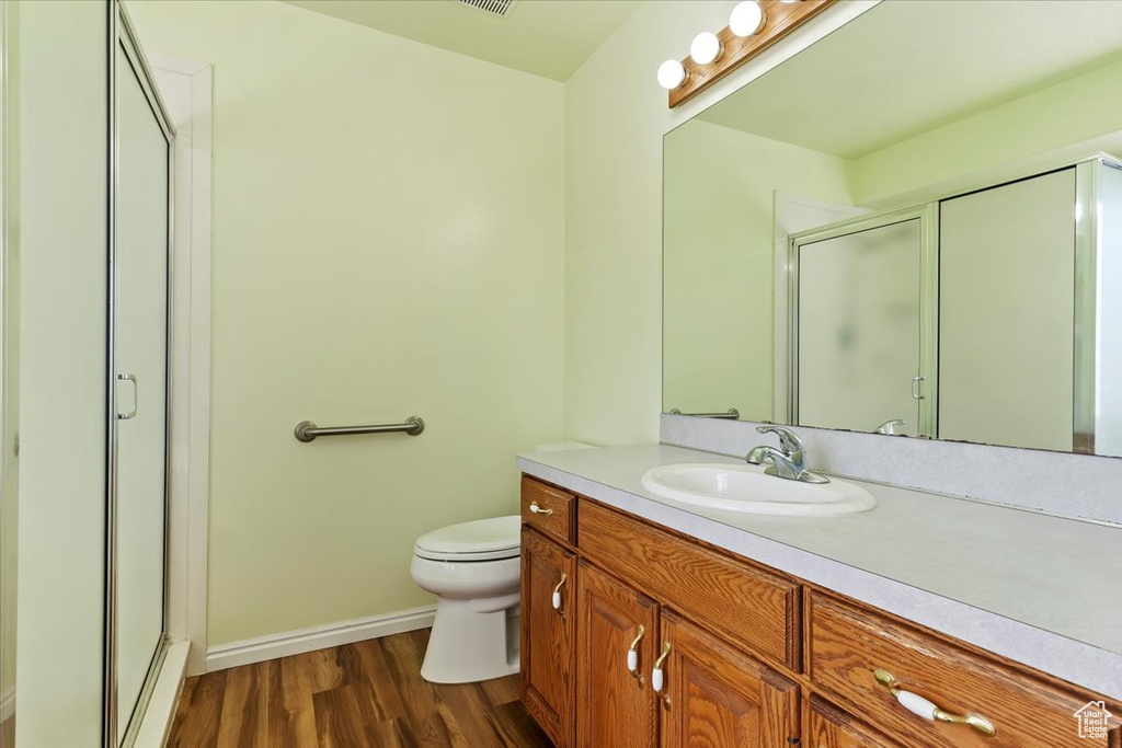 Bathroom featuring baseboards, toilet, wood finished floors, vanity, and a shower stall