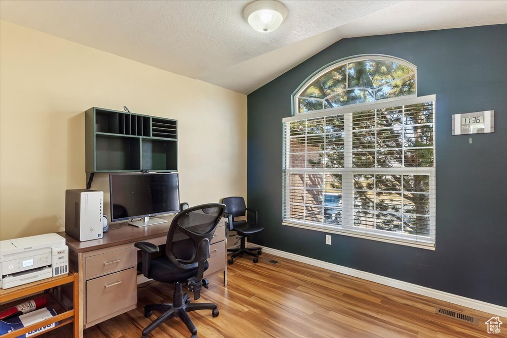 Office space with baseboards, visible vents, lofted ceiling, wood finished floors, and a textured ceiling