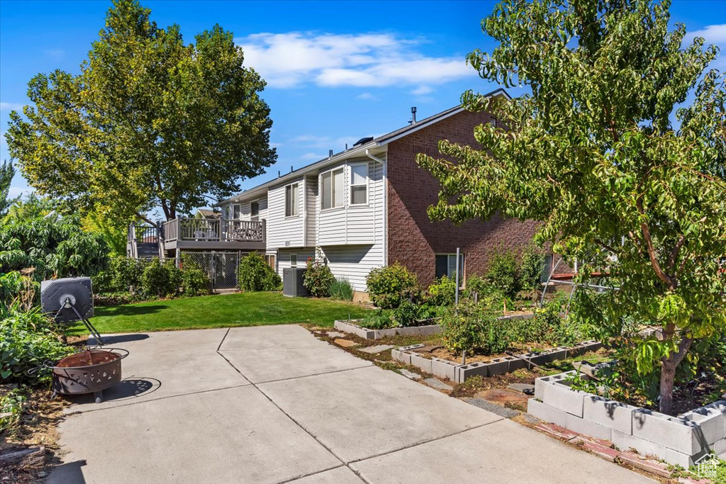 View of side of property with a deck, brick siding, a lawn, a vegetable garden, and a patio area