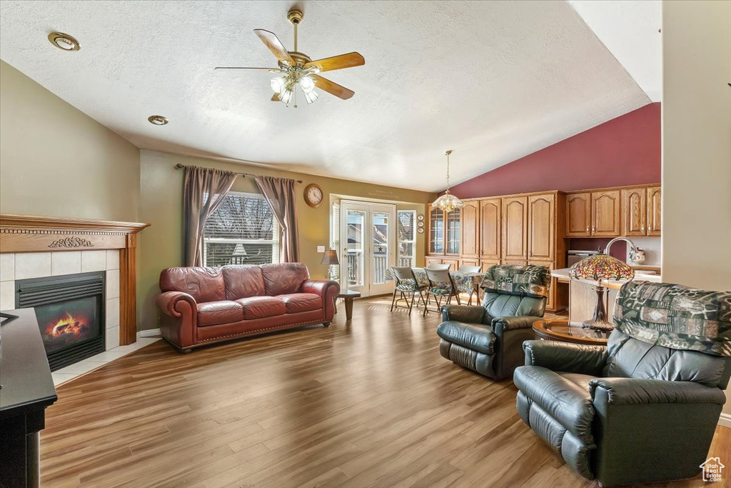 Living area with vaulted ceiling, a textured ceiling, a fireplace, and light wood-style floors