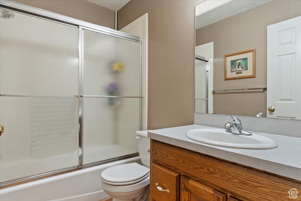 Full bathroom featuring toilet, bath / shower combo with glass door, and vanity