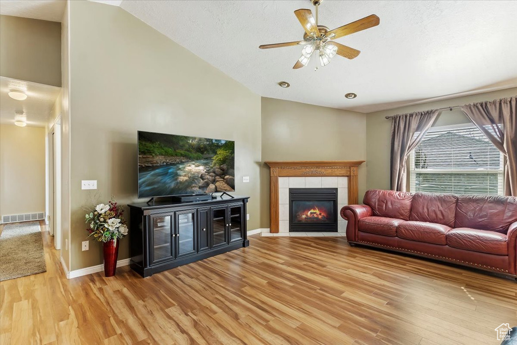 Living area with visible vents, baseboards, vaulted ceiling, light wood-type flooring, and a tiled fireplace
