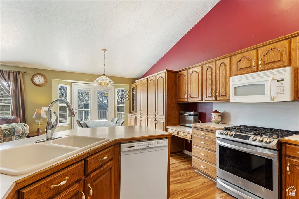 Kitchen featuring white appliances, decorative light fixtures, vaulted ceiling, light wood-style floors, and a sink