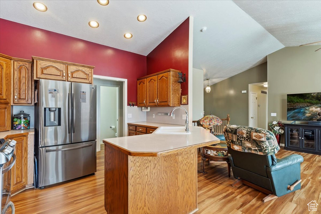 Kitchen with lofted ceiling, a sink, light countertops, light wood-type flooring, and stainless steel fridge
