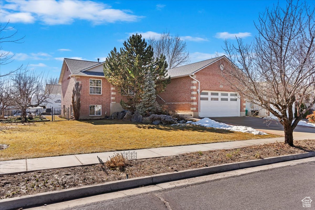 View of front of home featuring a garage, driveway, brick siding, and a front lawn