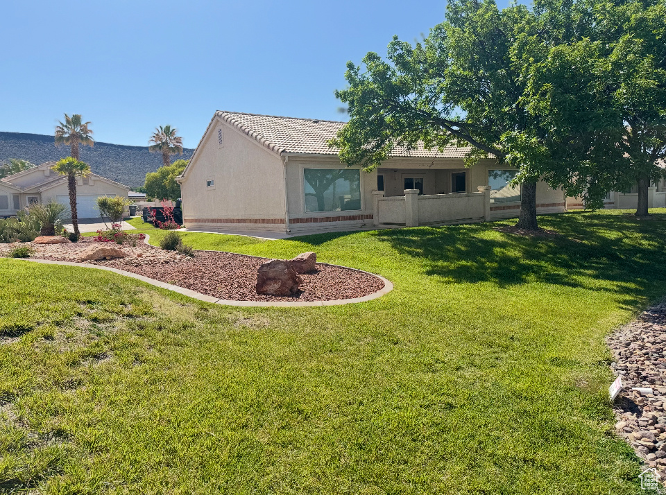 Back of property featuring a tiled roof, a lawn, and stucco siding