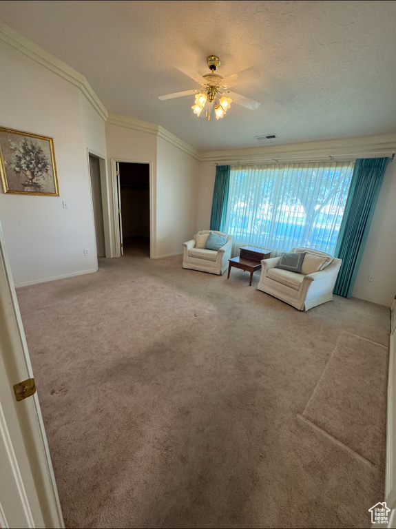 Living area with carpet flooring, a ceiling fan, crown molding, a textured ceiling, and baseboards