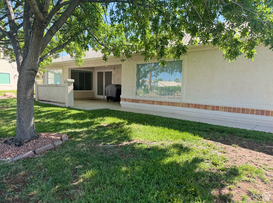 Rear view of property featuring stucco siding, a yard, and a patio