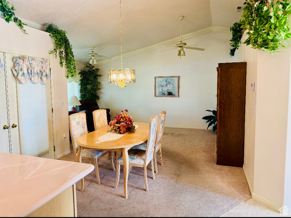 Dining room with light colored carpet, a ceiling fan, vaulted ceiling, crown molding, and a chandelier