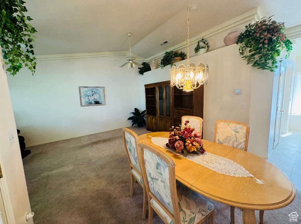 Carpeted dining space with a chandelier, ceiling fan, crown molding, and vaulted ceiling