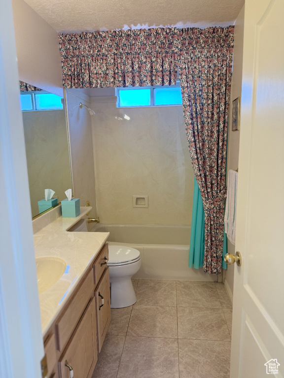 Bathroom with a textured ceiling, tile patterned floors, toilet, vanity, and shower / bath combination with curtain