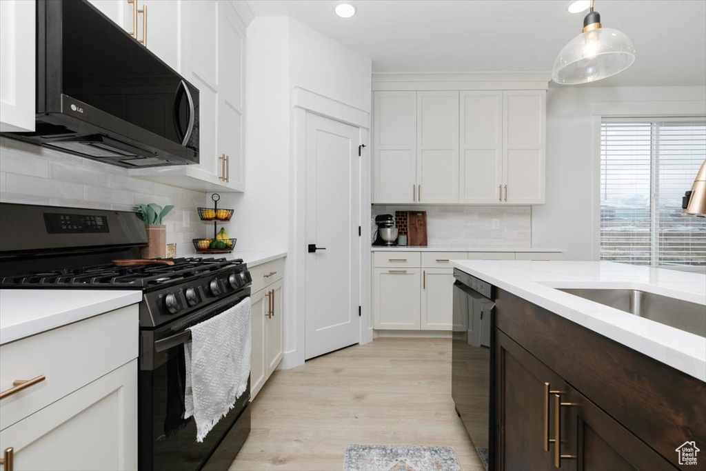 Kitchen with light countertops, backsplash, light wood-style floors, white cabinetry, and black appliances