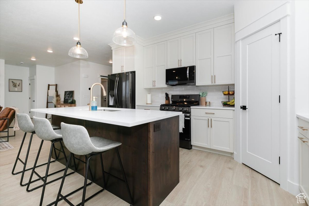 Kitchen featuring light wood-style flooring, a kitchen breakfast bar, light countertops, appliances with stainless steel finishes, and tasteful backsplash