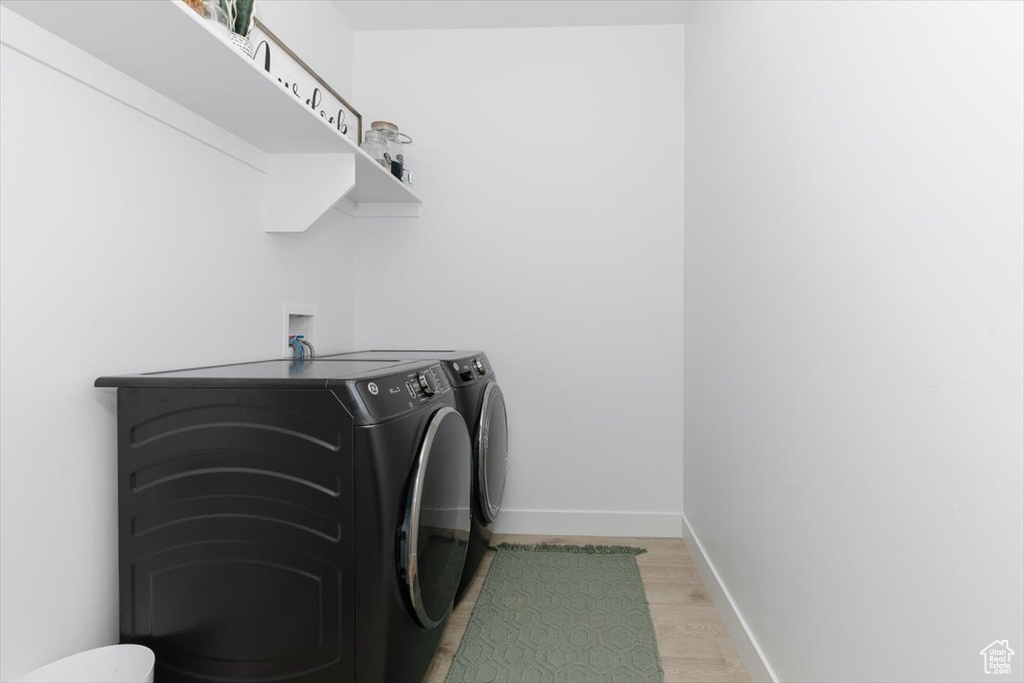 Washroom with light wood-type flooring, washer and dryer, laundry area, and baseboards