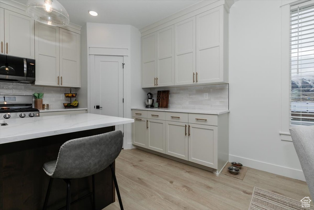 Kitchen featuring baseboards, light wood-style flooring, appliances with stainless steel finishes, a breakfast bar, and backsplash