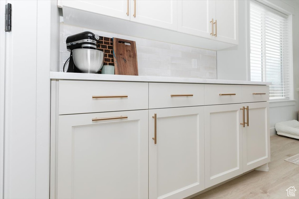 Interior details featuring light wood-style floors, light countertops, white cabinets, and decorative backsplash