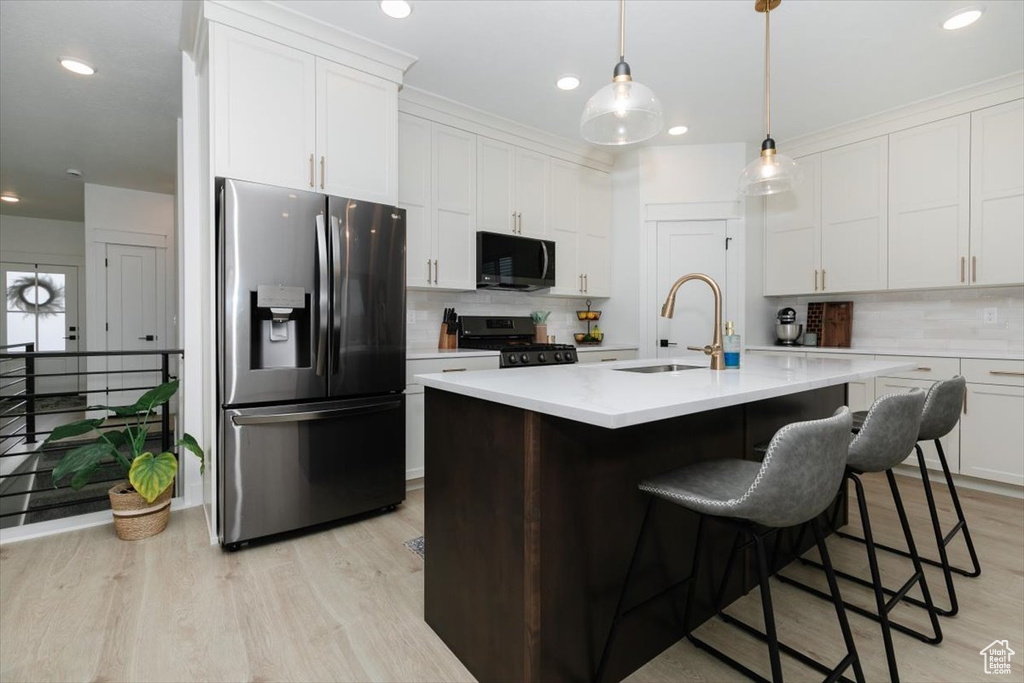 Kitchen featuring light wood finished floors, white cabinets, appliances with stainless steel finishes, light countertops, and a sink