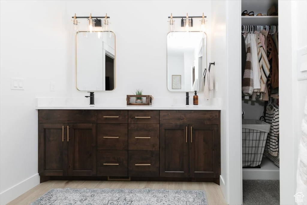 Full bathroom featuring double vanity, baseboards, a sink, and wood finished floors