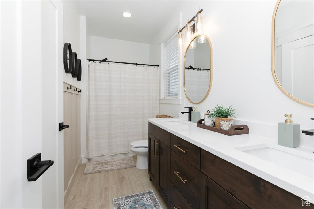 Full bathroom with double vanity, wood finished floors, a sink, and toilet