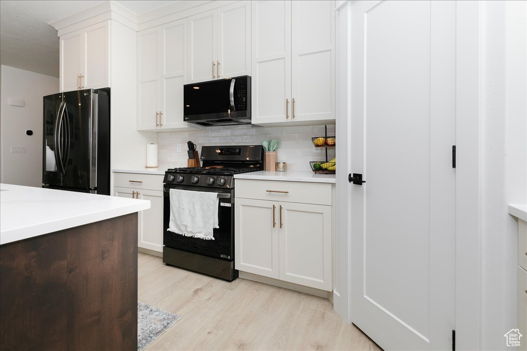 Kitchen featuring light wood finished floors, light countertops, black refrigerator with ice dispenser, decorative backsplash, and gas range