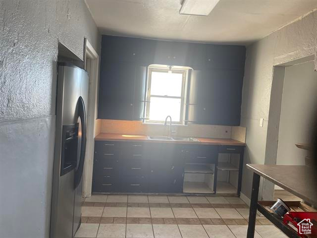 Kitchen featuring a textured wall, a sink, stainless steel refrigerator with ice dispenser, and light tile patterned floors